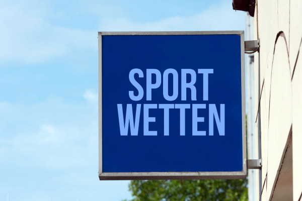 Nasenschild mit der Aufschrift "Sportwetten" an einer Hauswand.
