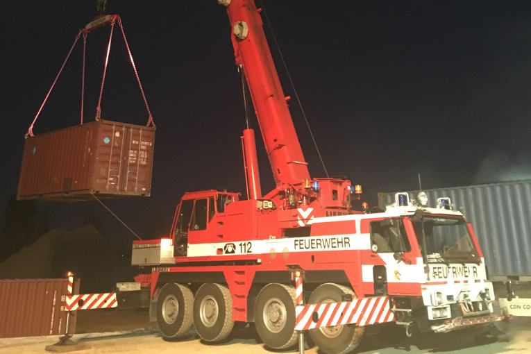 Ein Kran der Feuerwehr platziert Container am Fundort.