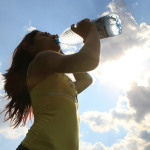 Eine Frau trinkt bei sommerlichem Wetter aus einer Wasserflasche.