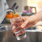 Eine Hand hält ein Glas unter einen laufenden Wasserhahn.