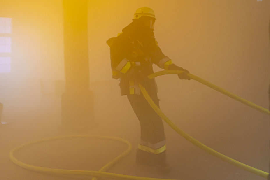 Bild © Daniel Mildner / Feuerwehr Nürnberg Einer der Einsatzkräfte zieht einen Löschschlauch in den verrauchten Raum., Bild © Daniel Mildner / Feuerwehr Nürnberg