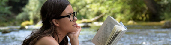 Eine Frau sitzt am Fluss und liest ein Buch.