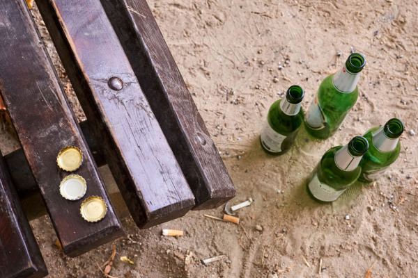 Leere Bierflaschen stehen vor einer Parkbank auf dem Boden.