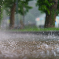 Starkregen prasselt auf einen unbefestigten Weg in einer Stadt, im Hintergrund Bäume.