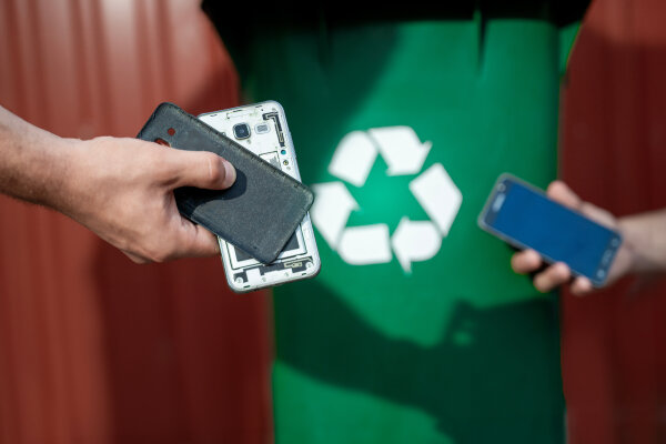 Eine Person hält ein altes, gebrauchtes Smartphone vor einer Recycling-Box.