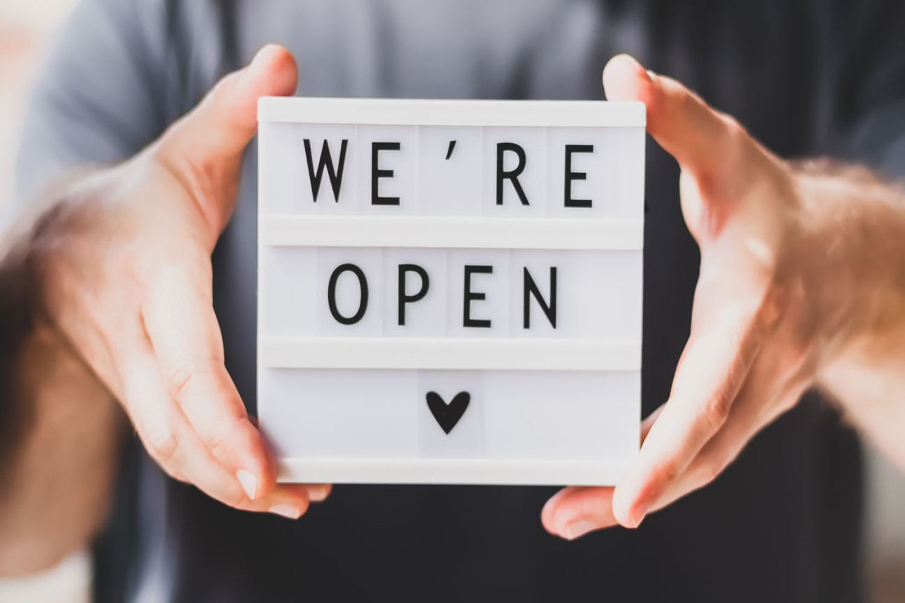 Bild © Dvoevnore / Adobestock Ein Mann hält eine kleine Lightbox mit dem Schriftzug "We're open" in die Kamera., Bild © Dvoevnore / Adobestock