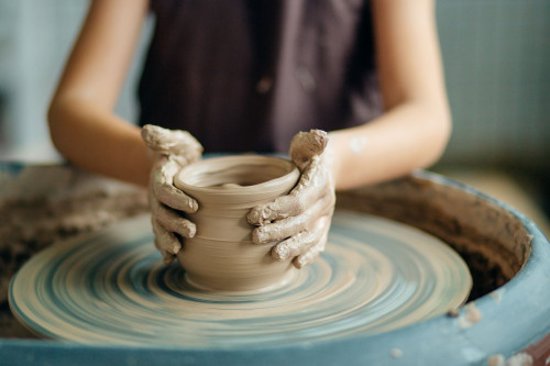 Zwei tonbeschmierte Hände formen ein Gefäß aus einem Stück Ton auf einer Drehscheibe .
